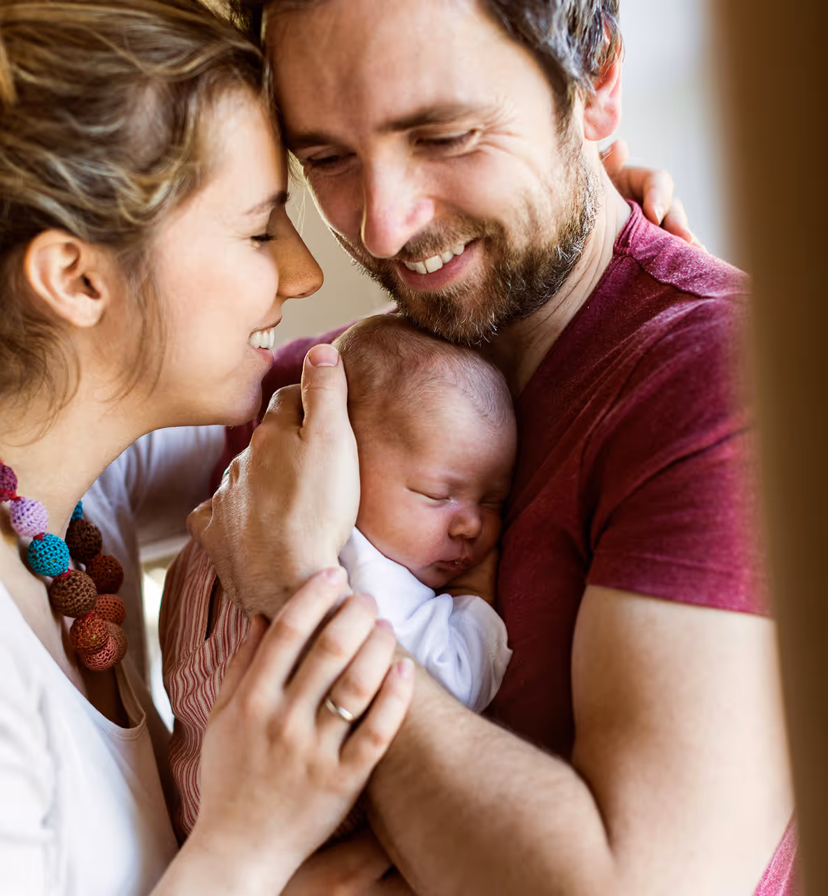 Un couple souriant tient tendrement leur bébé endormi contre la poitrine du père.