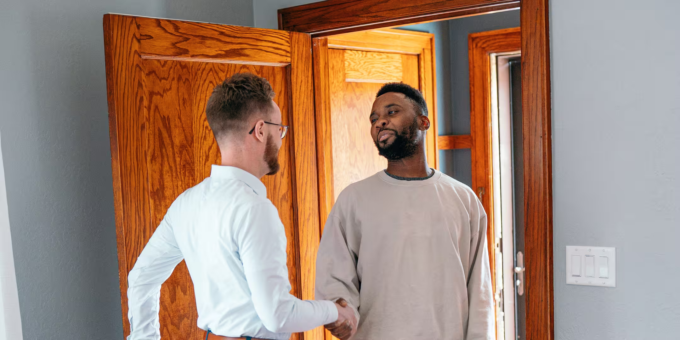 Deux hommes se serrant la main dans l'encadrement d'une porte en bois à l'intérieur d'une maison.