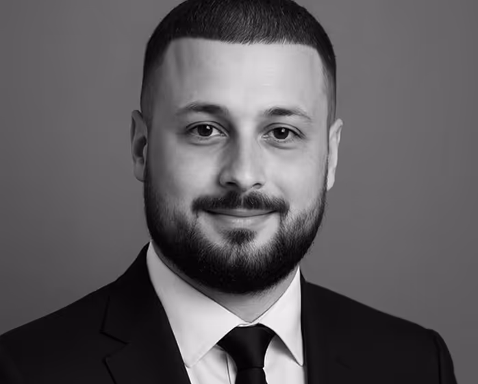 Portrait en noir et blanc d'un homme souriant portant un costume, une chemise blanche et une cravate noire.