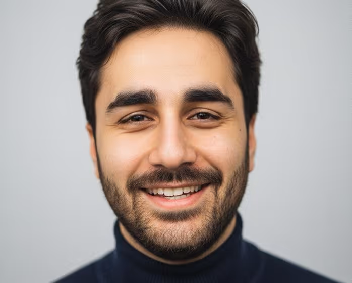 Portrait d'un homme souriant avec des cheveux foncés et une barbe, portant un col roulé noir.
