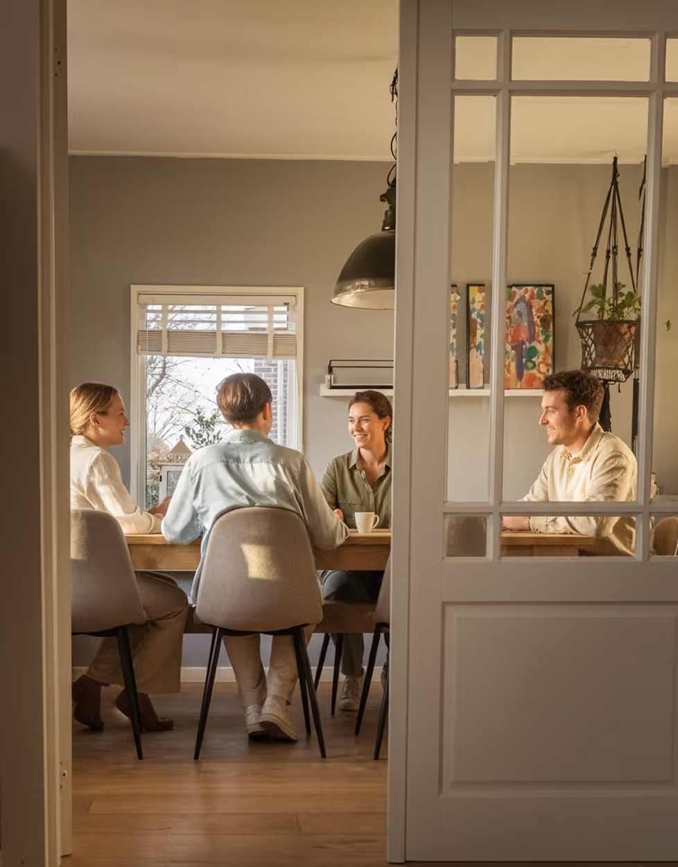 Quatre personnes assises autour d'une table en bois dans une salle à manger lumineuse, en conversation joyeuse.
