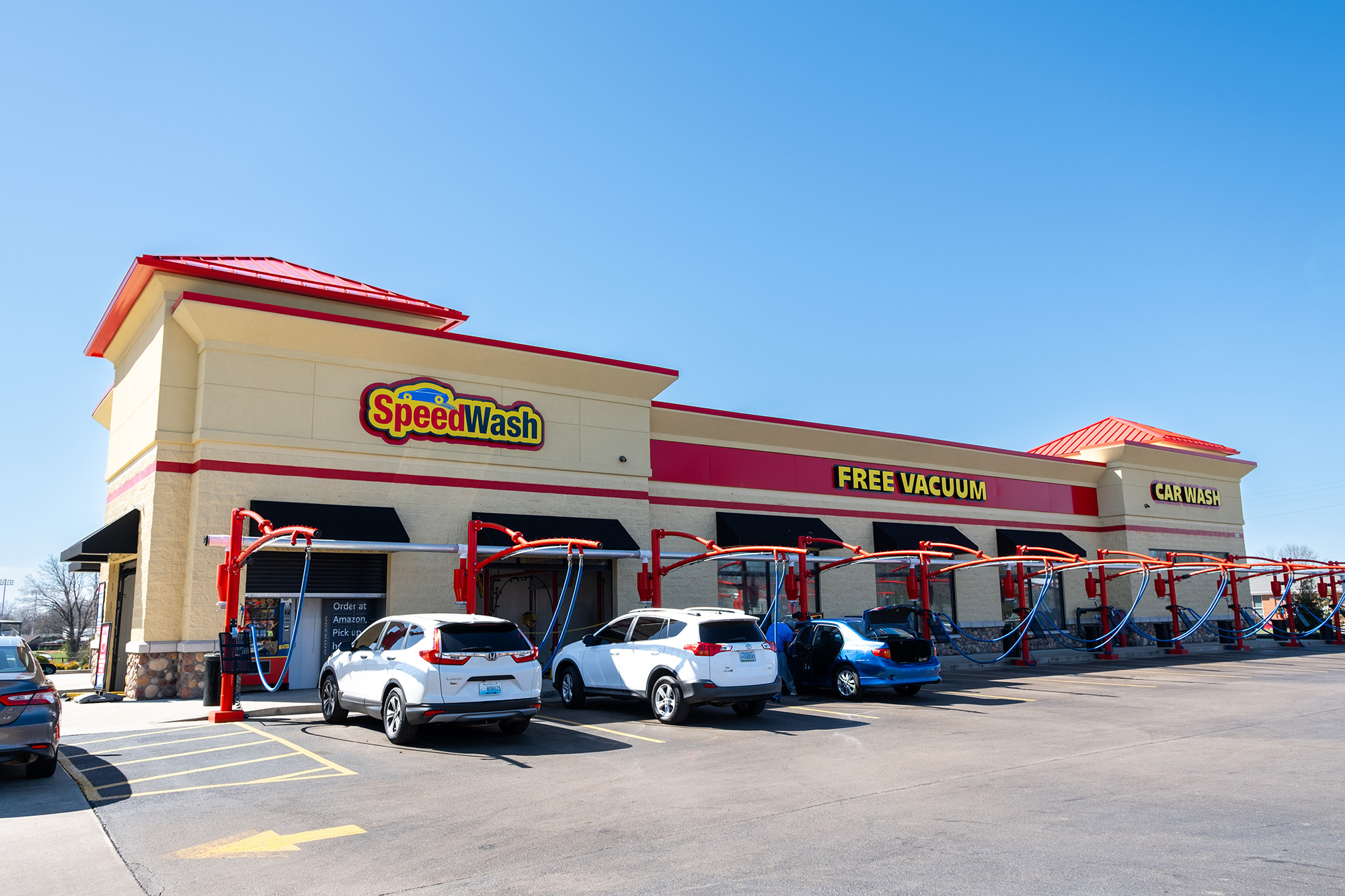 SpeedWash car wash with multiple vacuum stations and cars parked under clear blue sky.