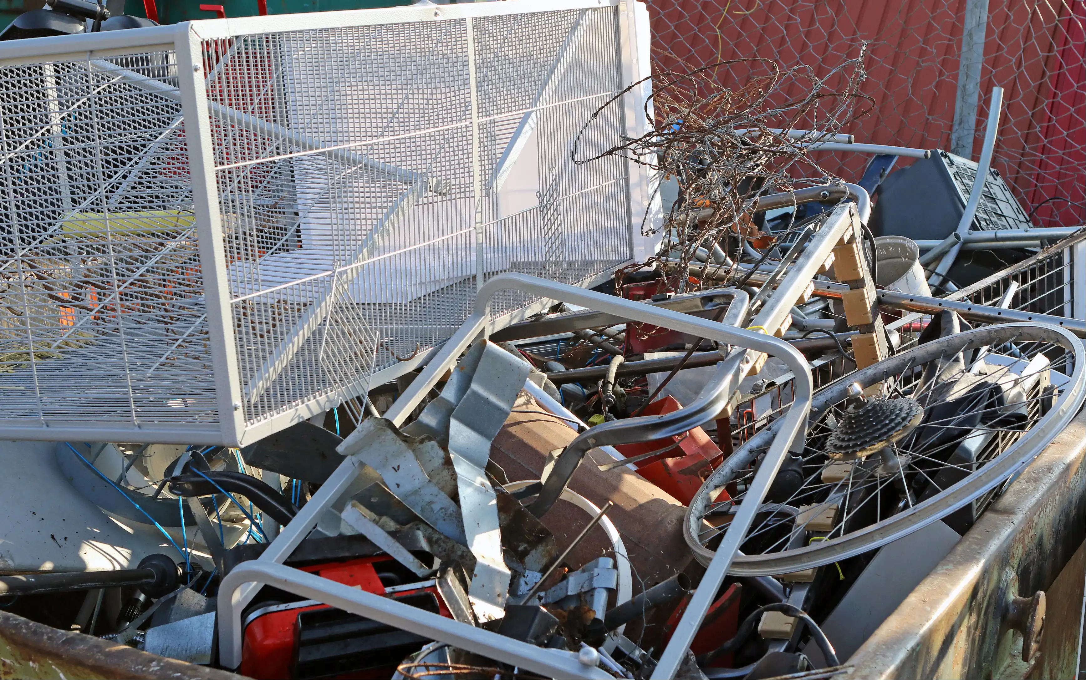 Pile of metal junk including wire mesh, bicycle wheel, pipes, and other scrap materials in a container.
