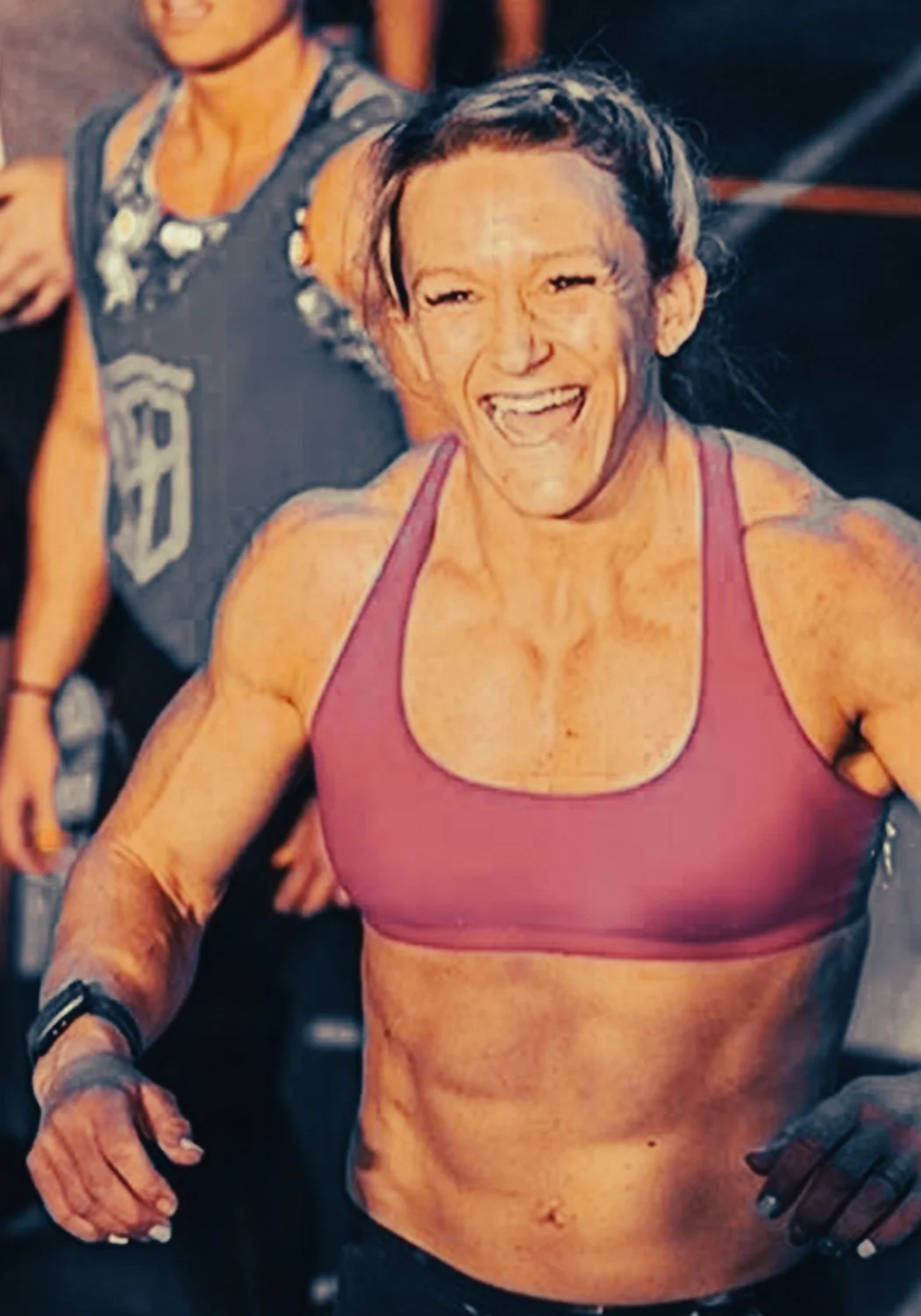 Muscular woman smiling and wearing a purple sports bra during a workout or competition.