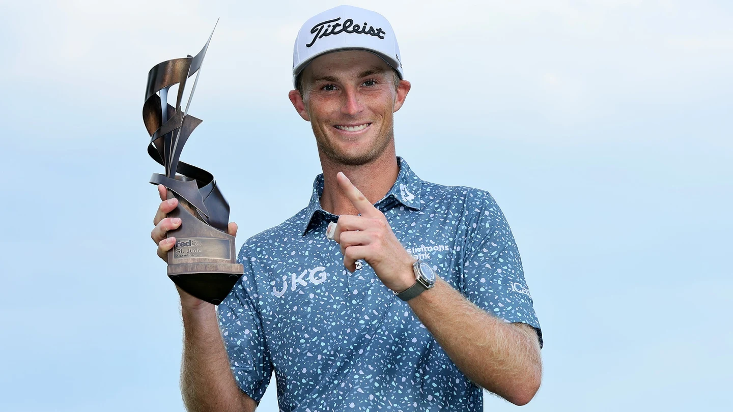 Smiling golfer holding a twisted metal trophy and pointing upward against a blue sky.