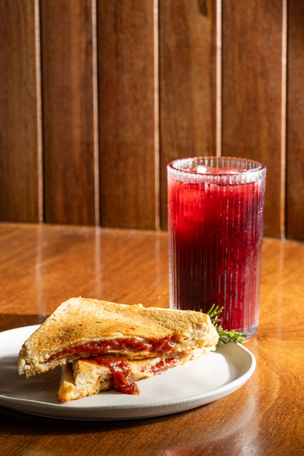 Sanduíche tostado e suco vermelho sobre mesa de madeira