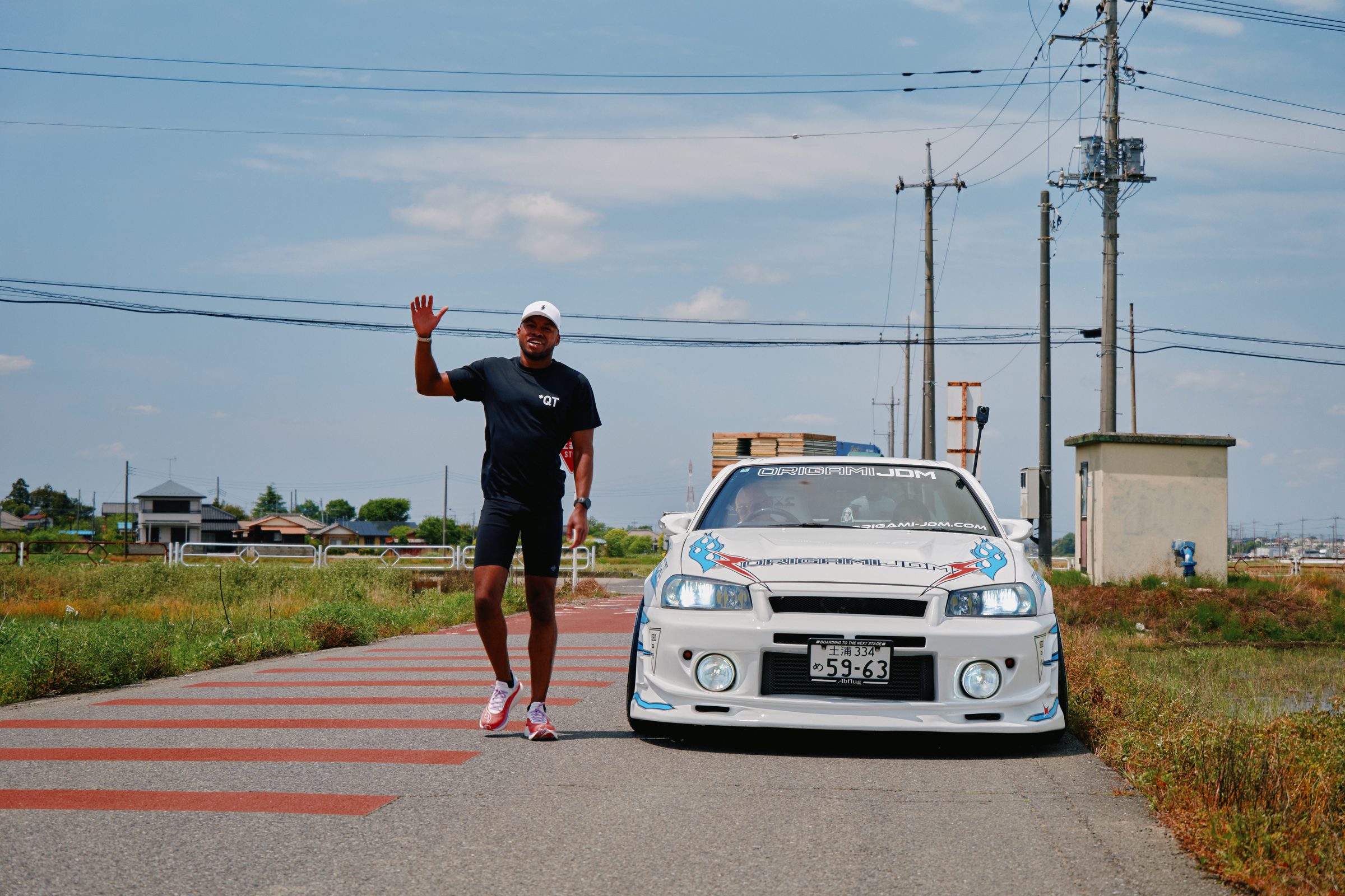 QuHarrison Terry in a *QT shirt beside a white Skyline, Japan