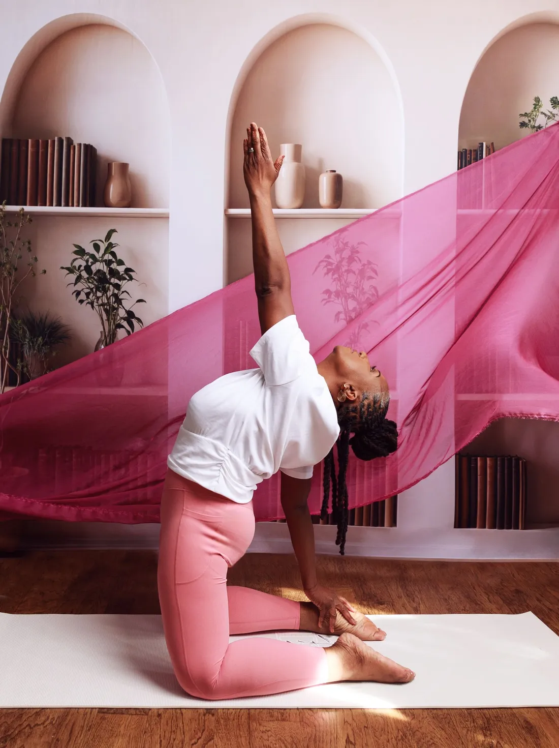 Dianne Adkins-Forte stretching into a kneeling backbend beneath flowing pink fabric