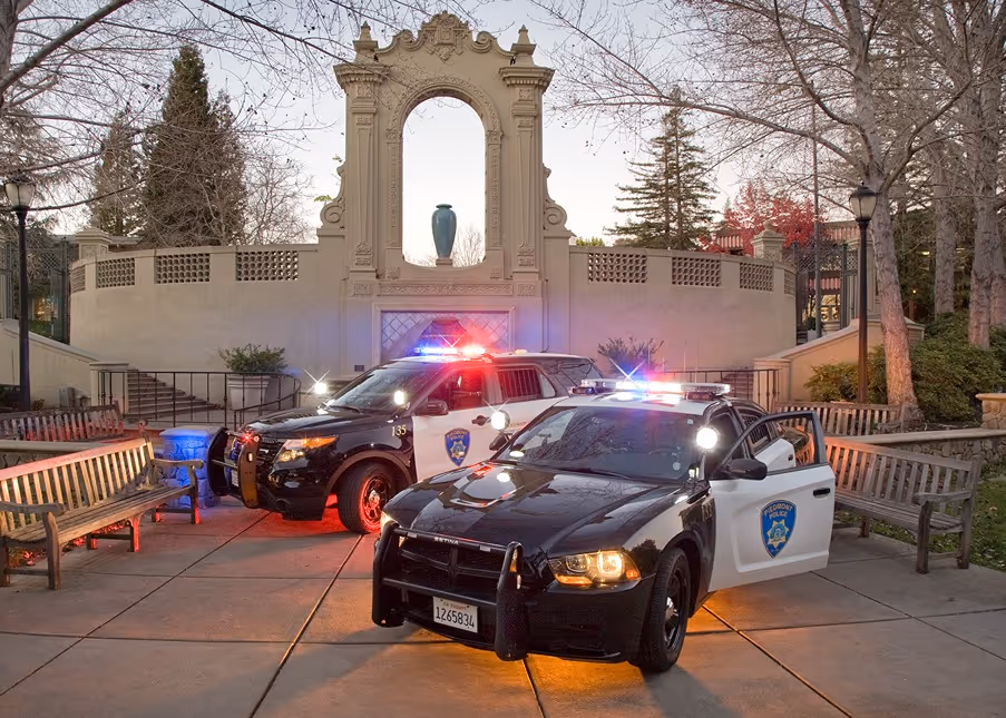 Two black and white police cars with flashing lights parked in a courtyard in front of a decorative archway.