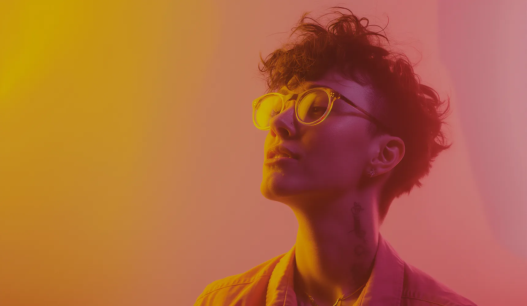 Person with short curly hair and glasses looking upward against a gradient orange and pink background.