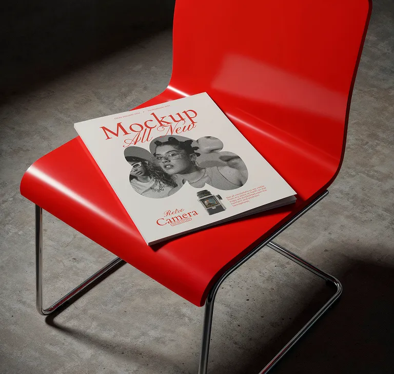 Magazine titled 'Mockup All New' with black-and-white photo of two people on cover, placed on a red chair with chrome legs on a gray floor.