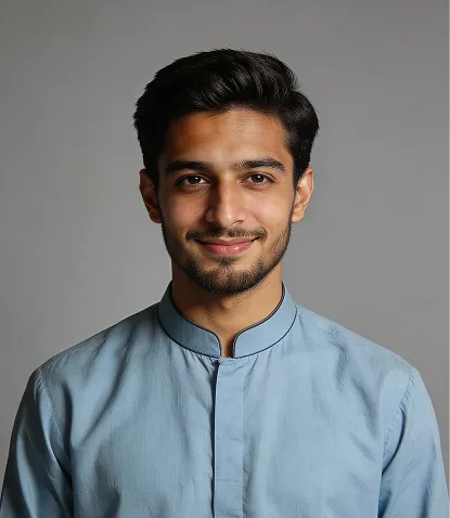 Portrait of a young man with dark hair and beard wearing a light blue shirt against a gray background.