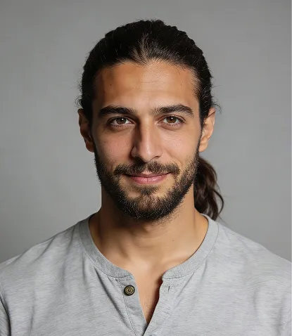 Portrait of a man with dark hair tied back and a beard, wearing a light gray shirt, against a plain gray background.