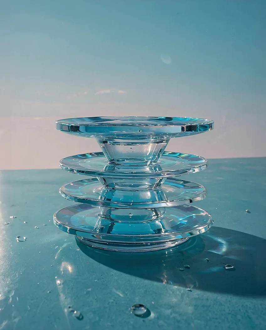 Stack of four clear glass dishes on a blue surface with water droplets and a soft blue background.
