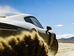 Silver sports car speeding on a desert road kicking up sand under a clear blue sky.