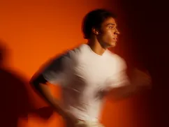 Blurred image of a young man in a white shirt running against an orange background.