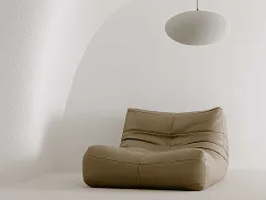 Modern beige lounge chair under a round ceiling lamp in a minimalist room with white walls.