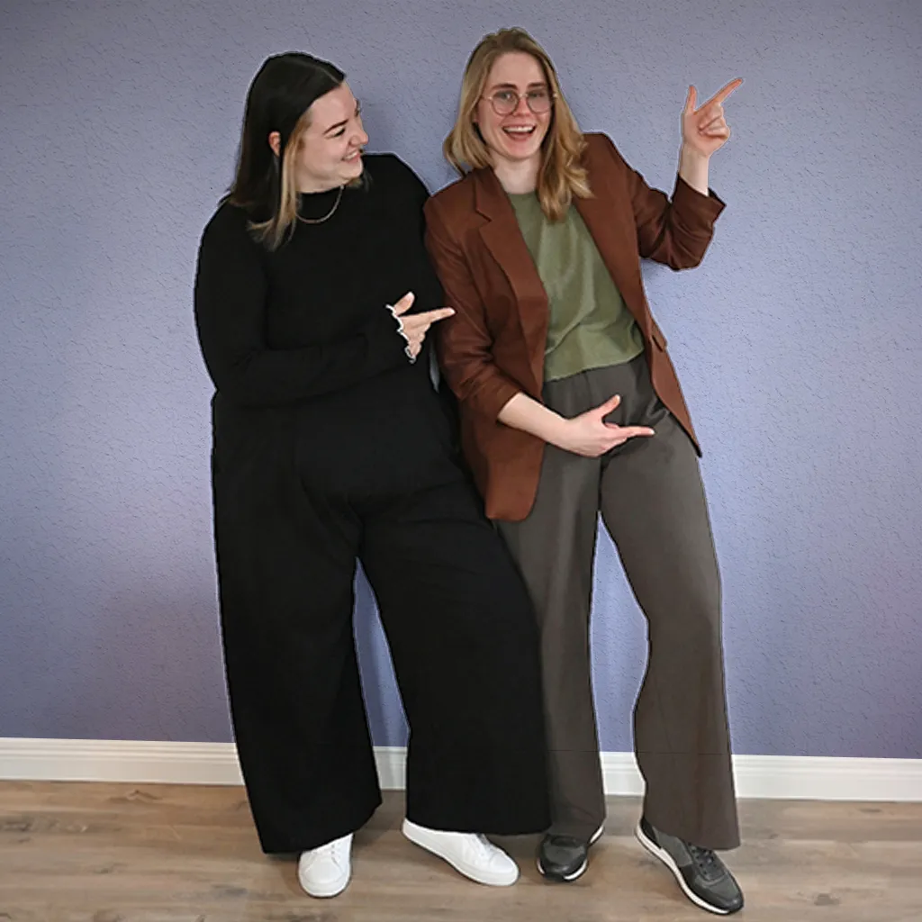 Lena und Elisabeth von Femvestory zeigen motiviert auf die Terminbuchung für ein kostenloses Erstgespräch zur persönlichen Finanzplanung.