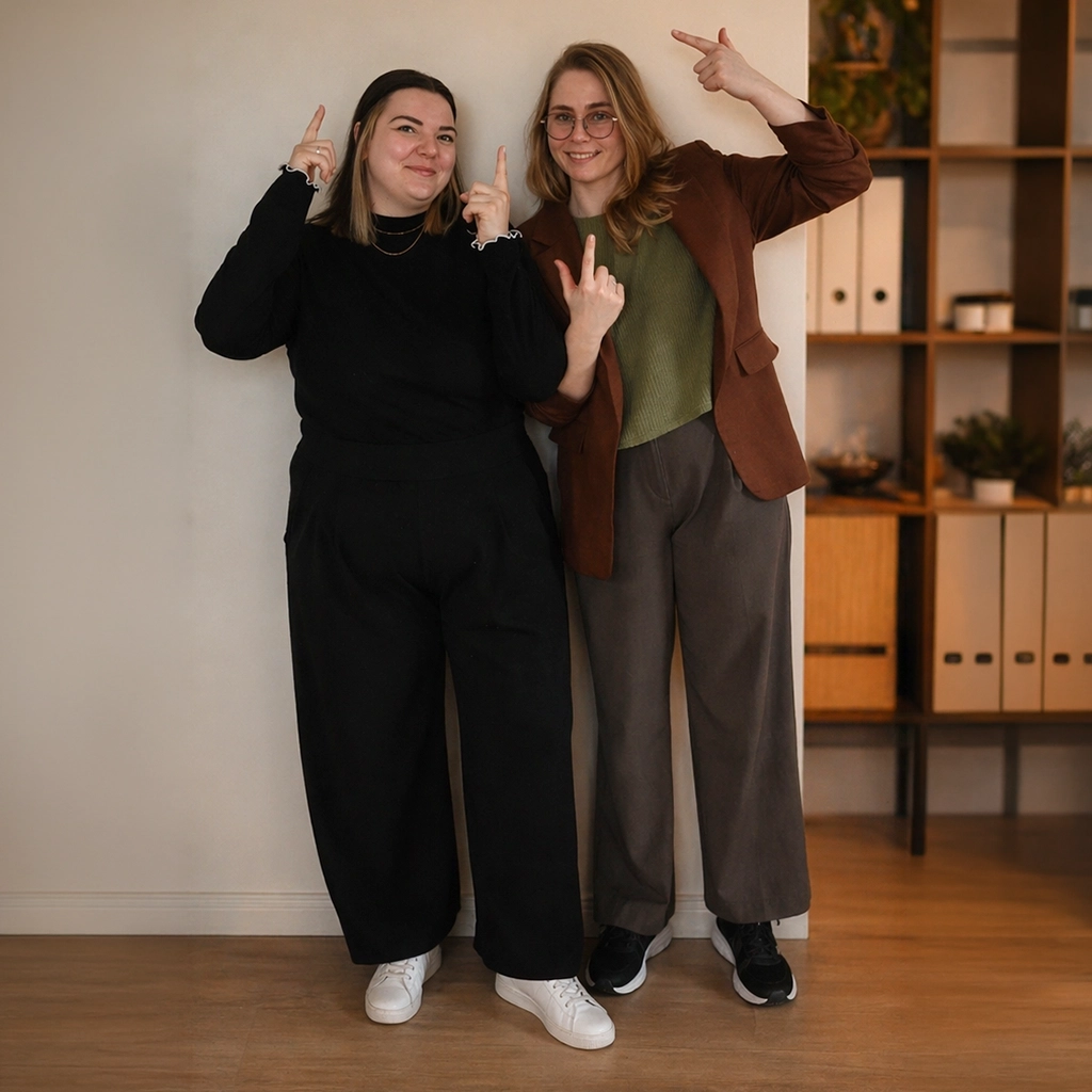 Lena und Elisabeth von Femvestory zeigen motiviert auf die Terminbuchung für ein kostenloses Erstgespräch zur persönlichen Finanzplanung.
