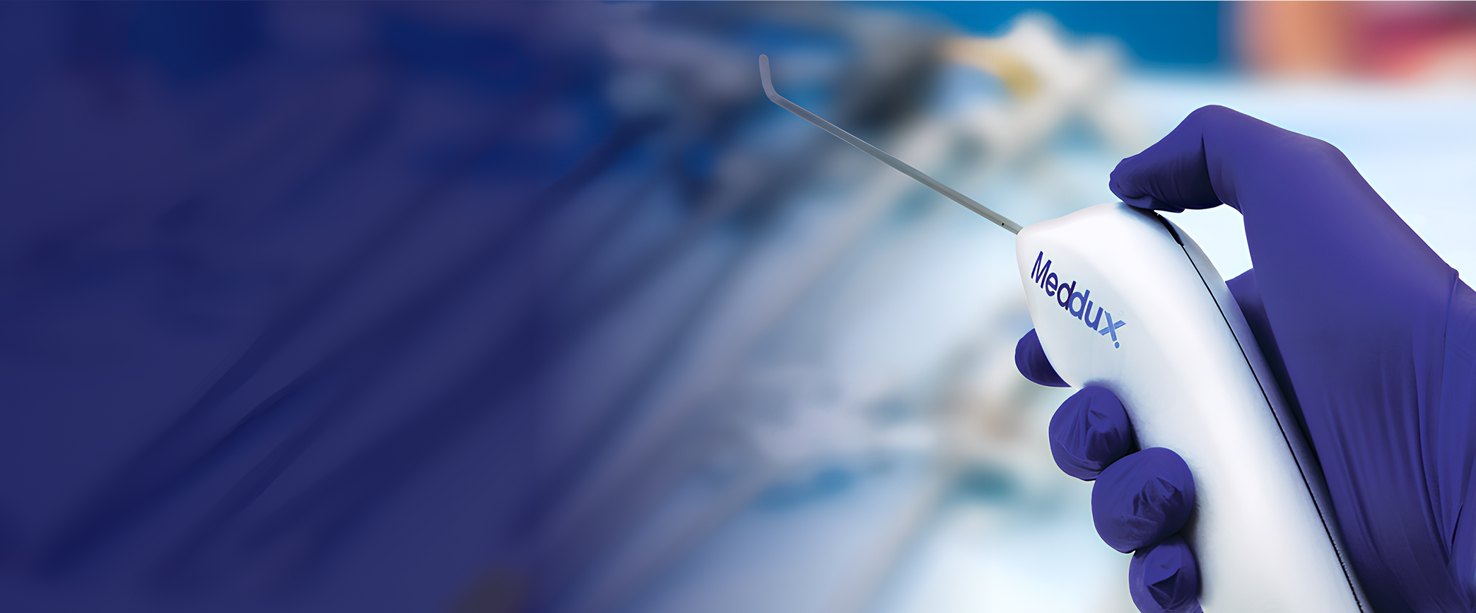 Hand in purple glove holding a Meddux medical device with a thin metal probe.
