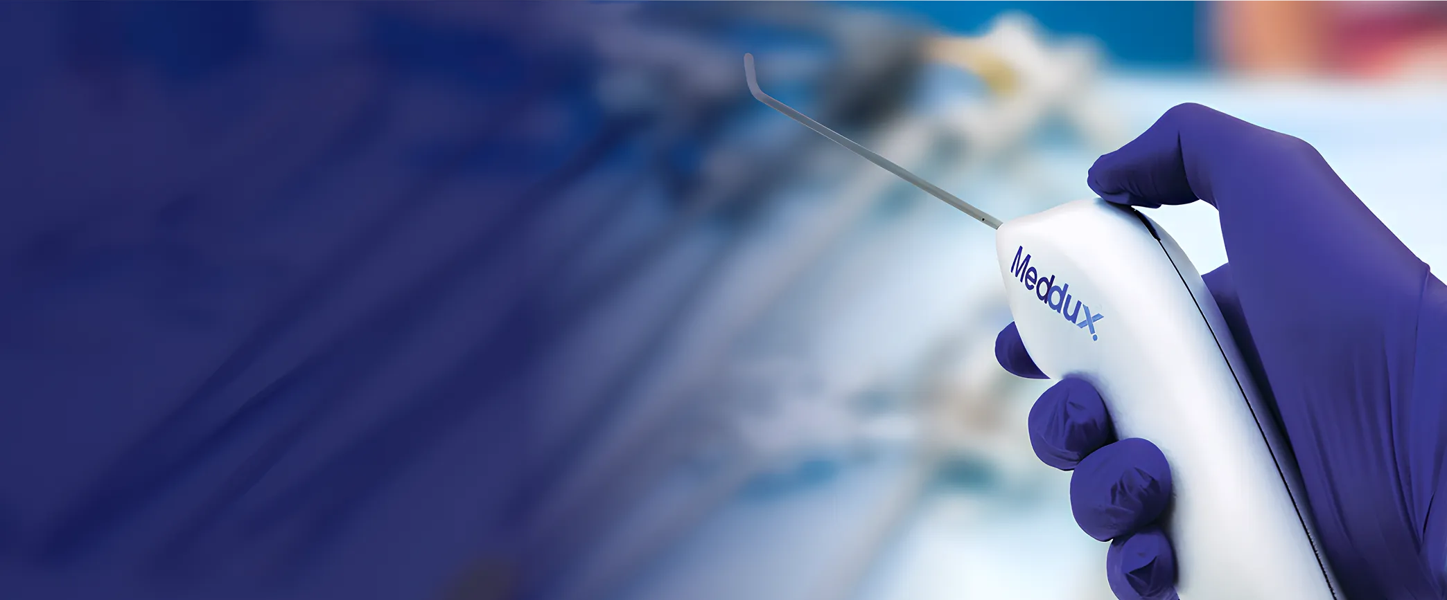 Hand in purple glove holding a Meddux medical device with a thin metal probe.