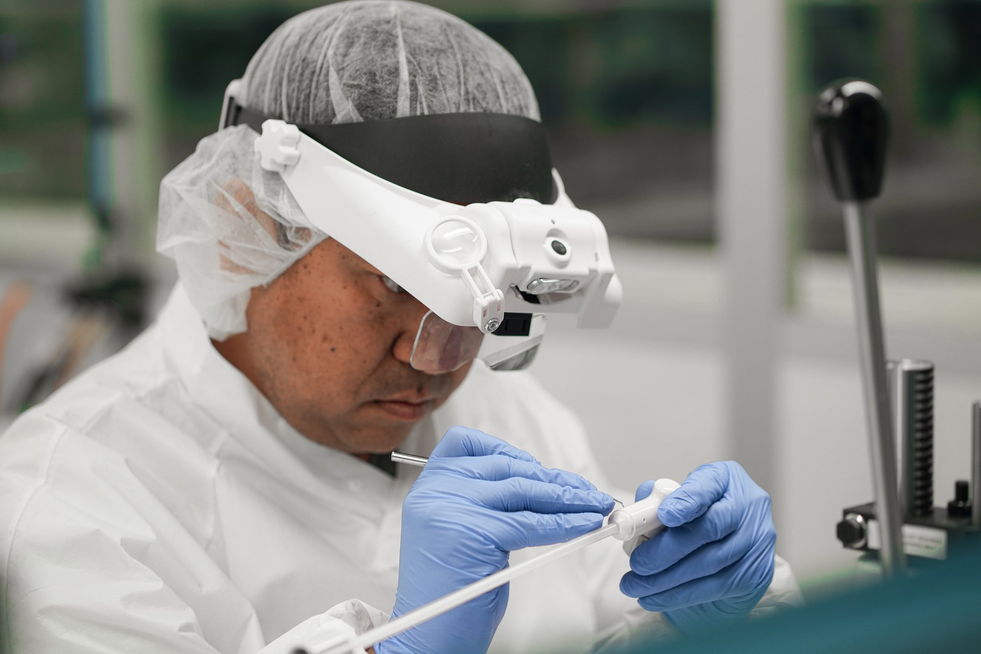 Technician with magnifying headset assembling a catheter device