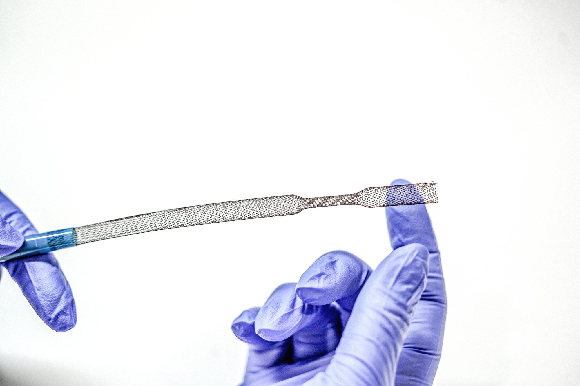 Gloved hands flexing a braided catheter shaft section