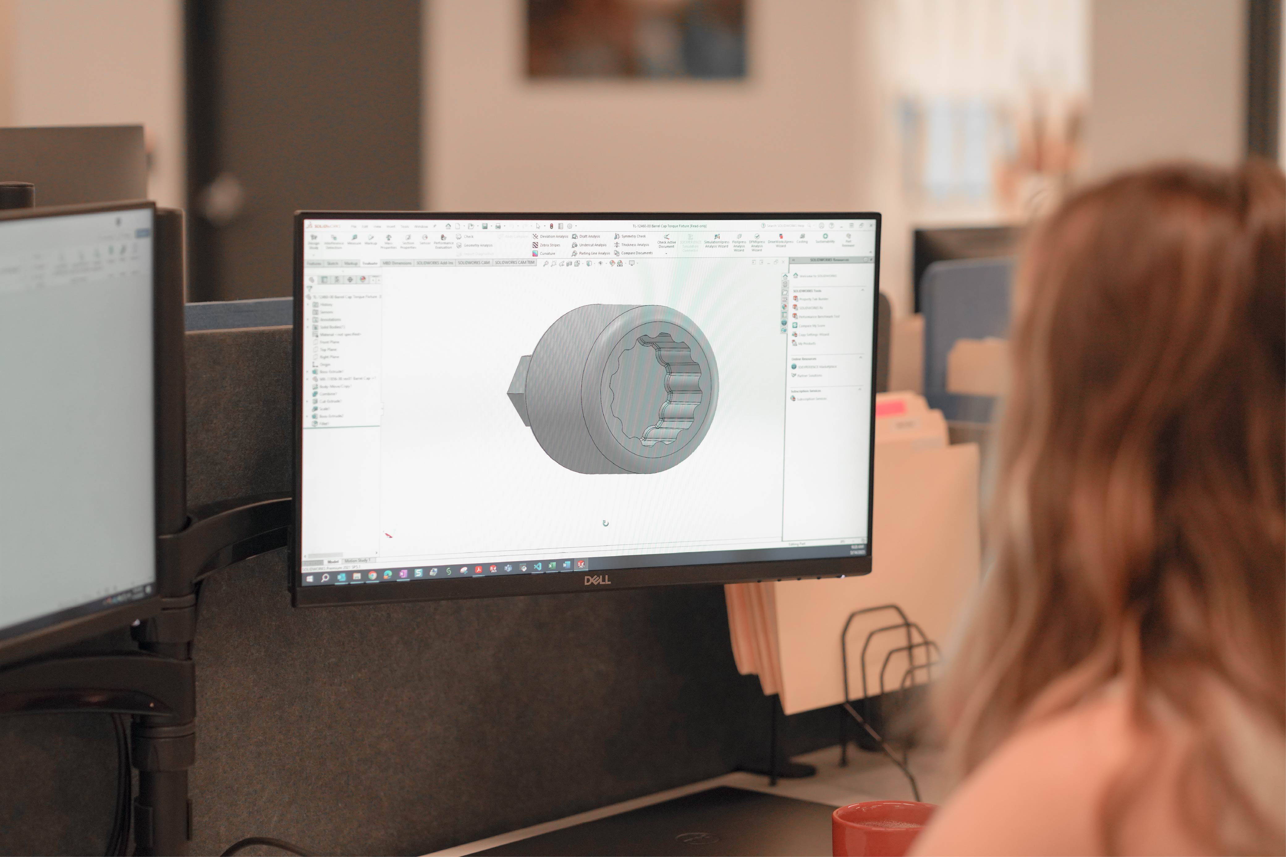 Person viewed from behind working at a desk, with a Dell monitor displaying a 3D CAD model of a mechanical fastener component in SOLIDWORKS