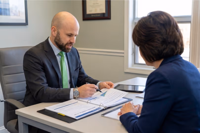 Chuck explaining documents with charts to a client across a desk in an office.
