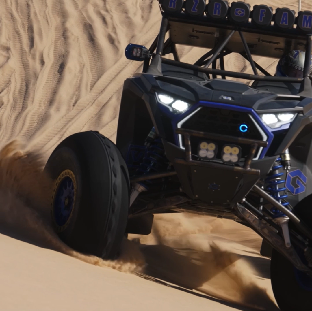 Off-road vehicle driving fast on sandy dunes, kicking up sand dust.