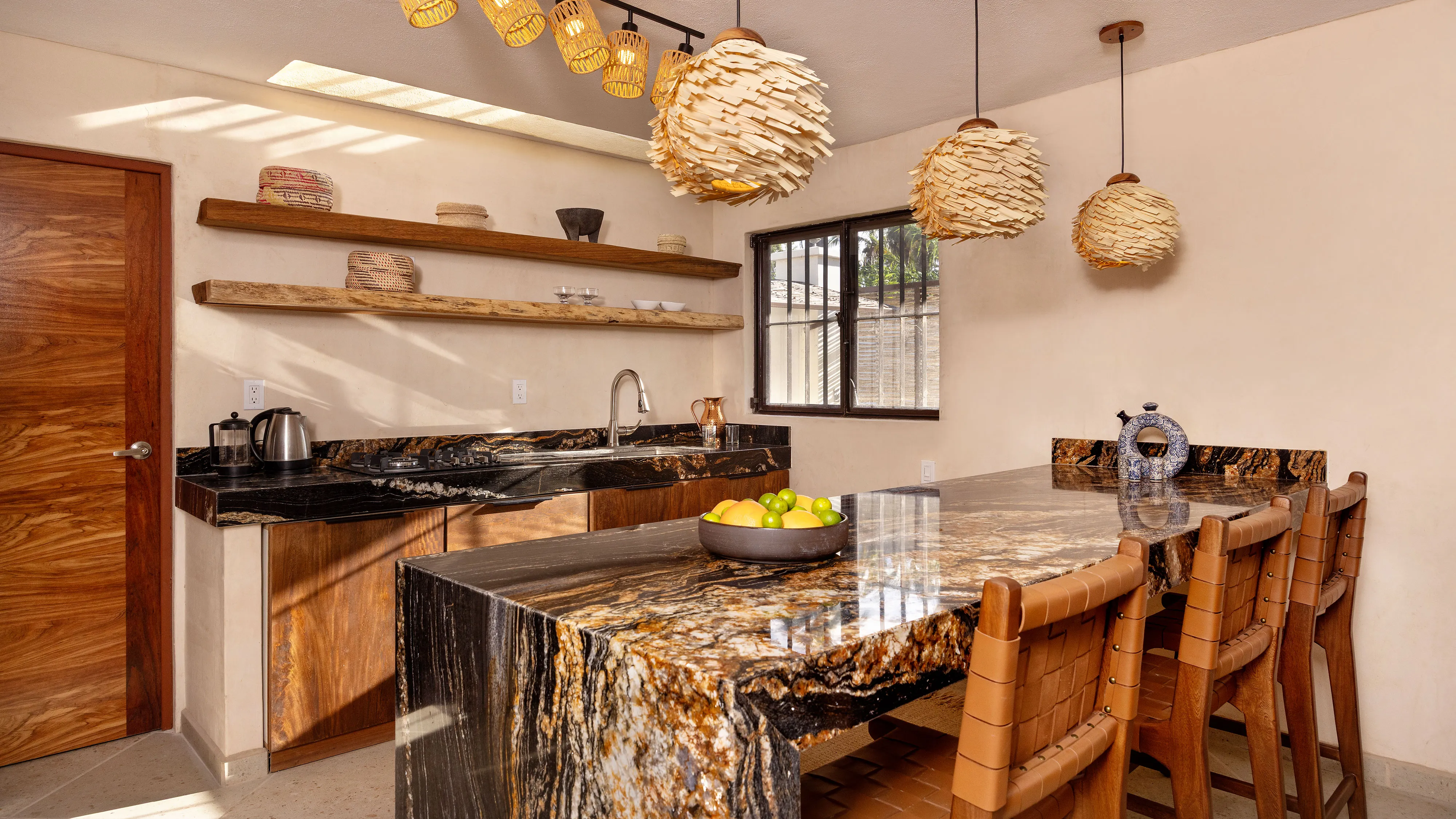Kitchen with black and gold marble countertops, wooden chairs, pendant lights, and shelves with decor.