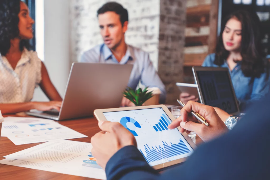 A person holding a tablet surrounded by others in a meeting