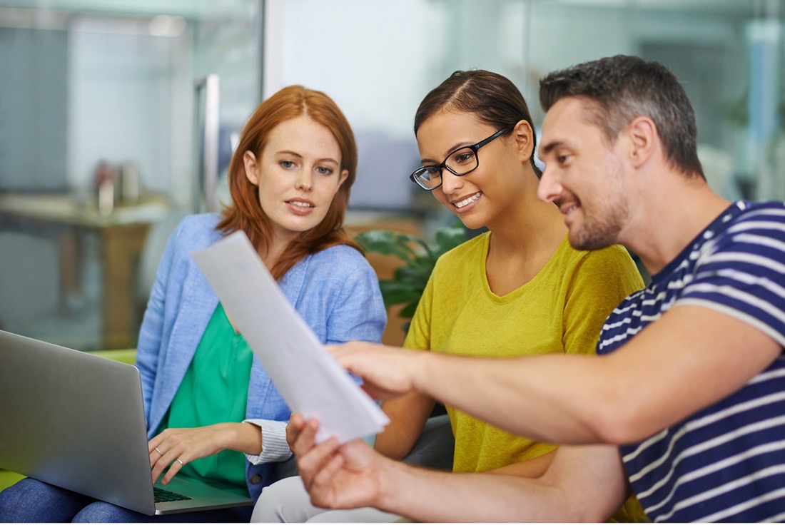 Three colleagues collaborate in an office, reviewing a document together with a laptop on the table.
