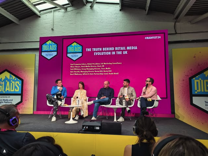 Panel of five speakers seated on stage discussing retail media evolution in the UK with bright magenta and yellow DIGIADS branding in the background.