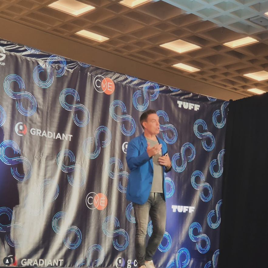 Man in a blue blazer speaking on stage with a backdrop featuring logos for Gradiant, CVE, and TUFF.
