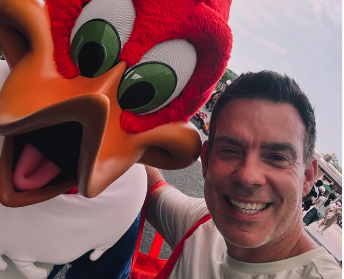 Smiling man taking a selfie with a person in a large Woody Woodpecker costume outdoors.