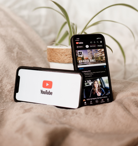 Two smartphones on a beige blanket, one displaying the YouTube logo and the other showing a YouTube app screen with video thumbnails.