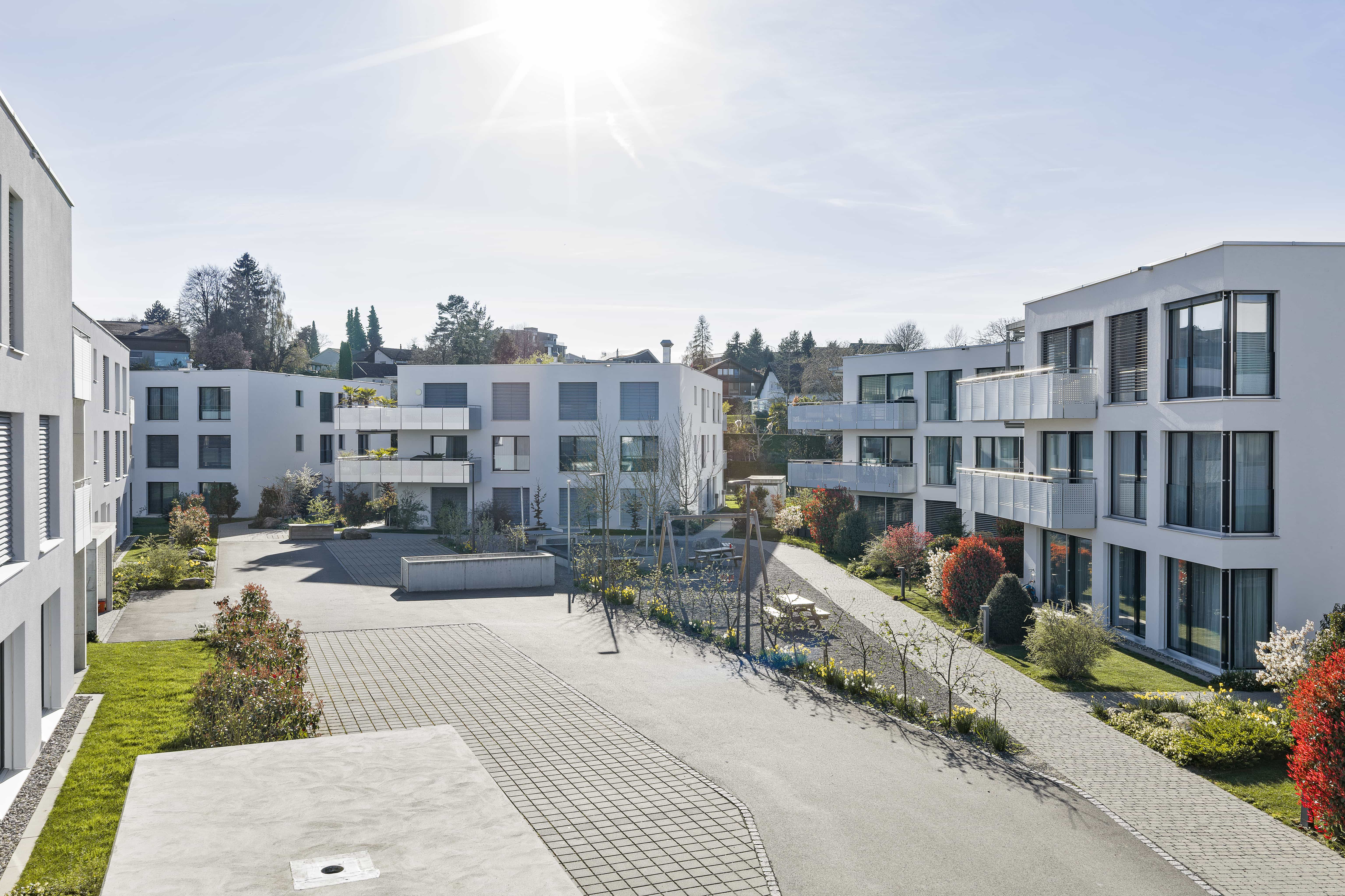 Moderne weiße Wohngebäude mit großen Fenstern und Balkonen an sonnigem Tag.
