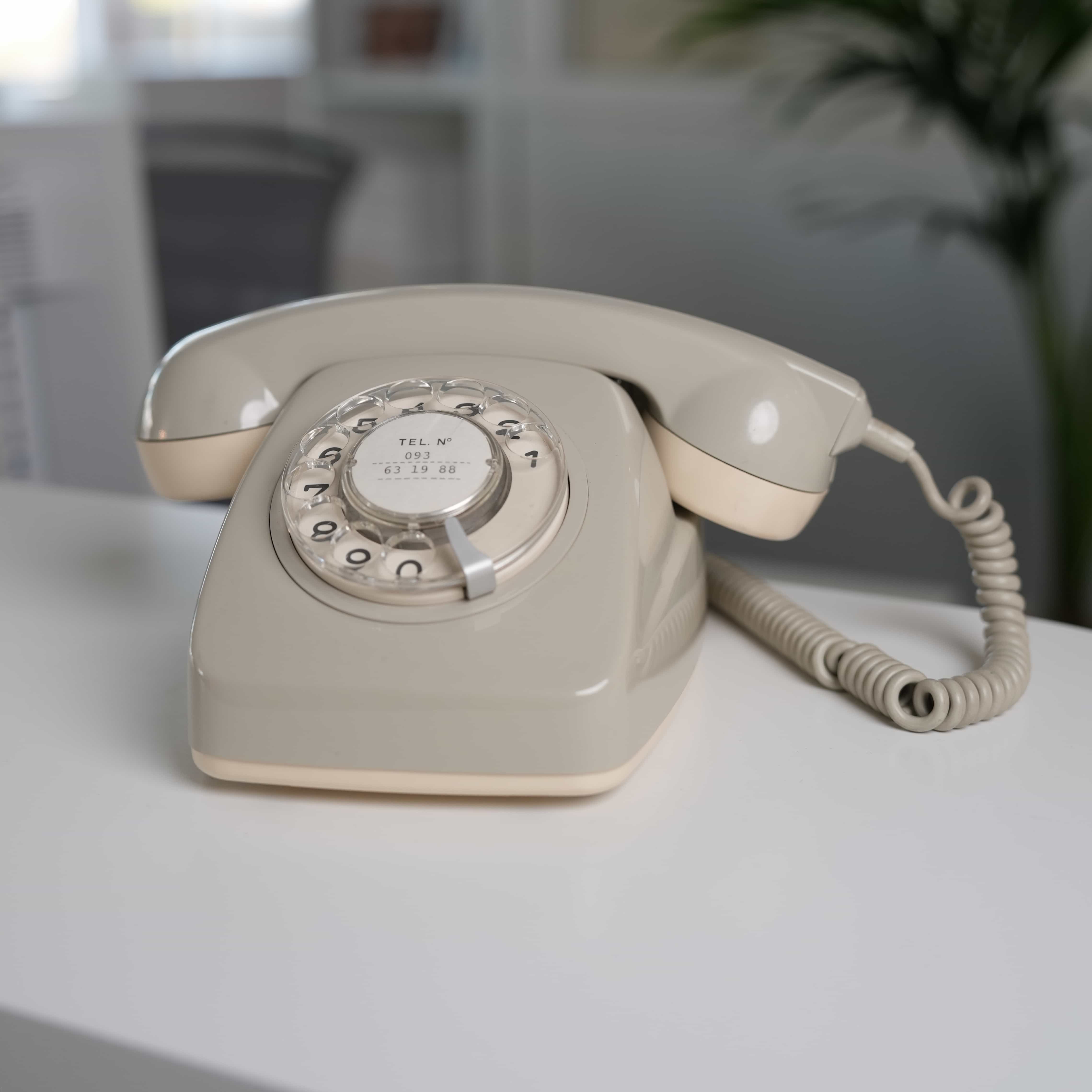 Beiger Retro-Wählscheibentelefon auf einem weißen Tisch vor unscharfem Hintergrund.