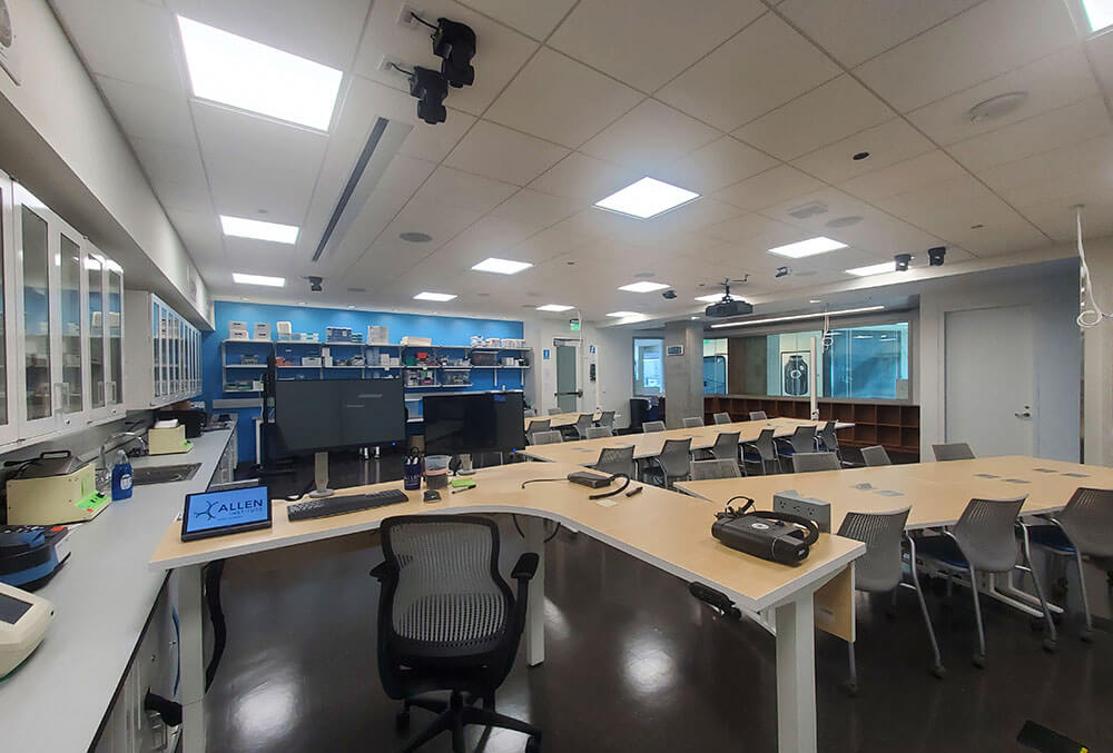 Modern office classroom with curved desks, ergonomic chairs, and blue shelving units overhead