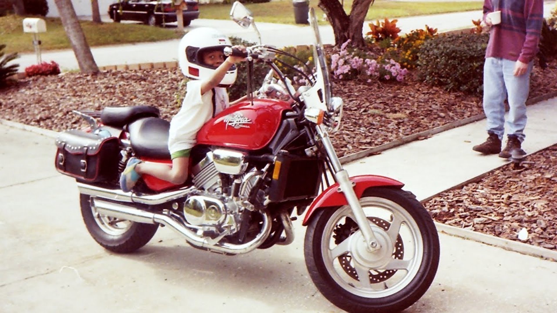 Person in white helmet and red jacket riding red and white motorcycle in residential driveway.