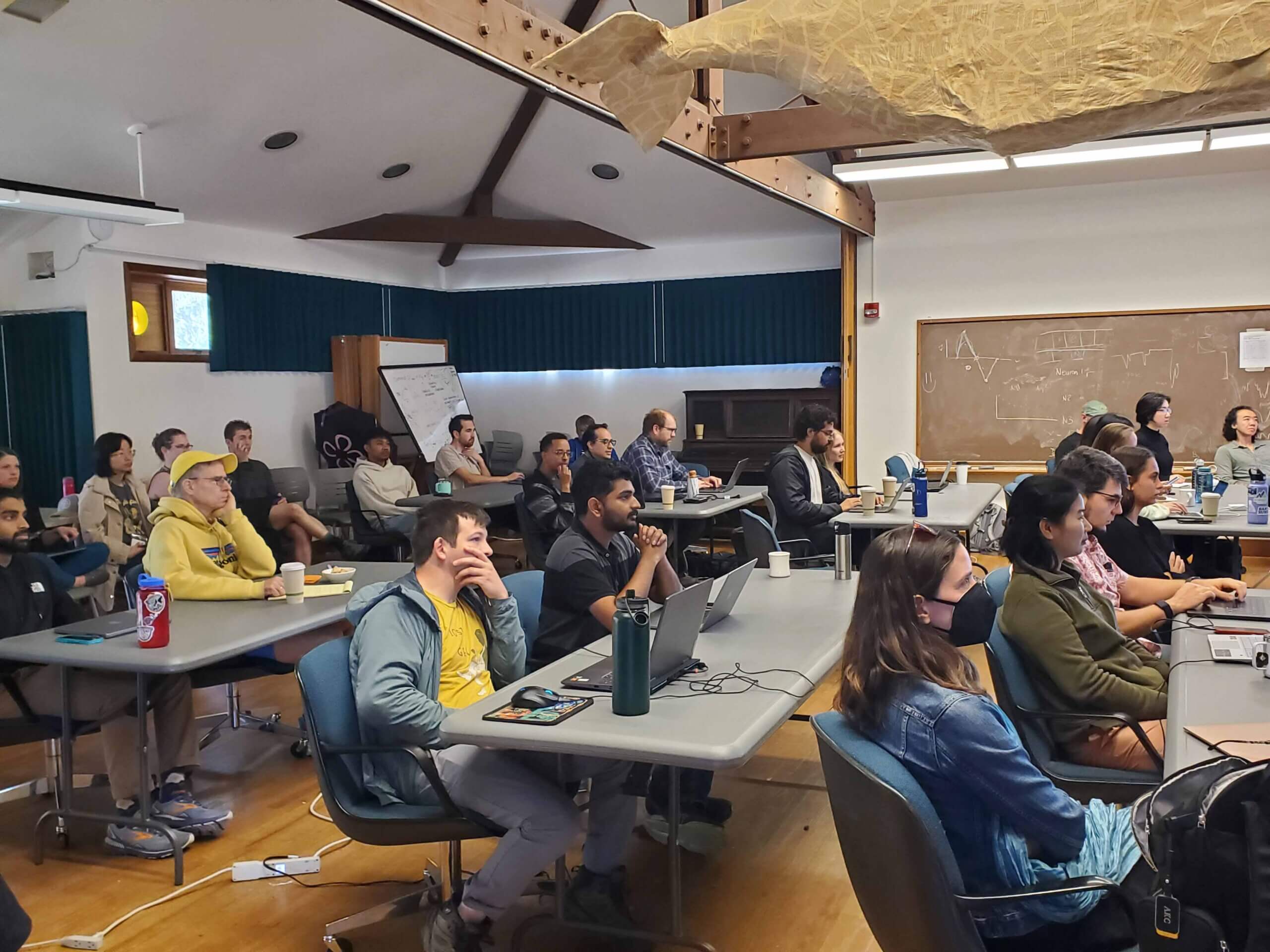 Large classroom full of students sitting at tables listening to lecture or presentation