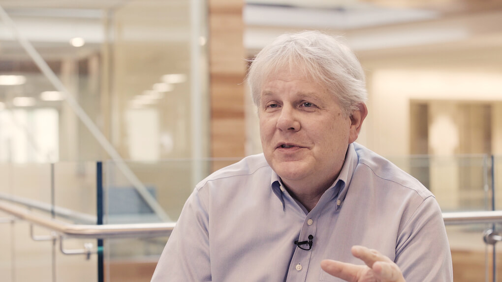 Senior man with white hair speaking in modern office building hallway