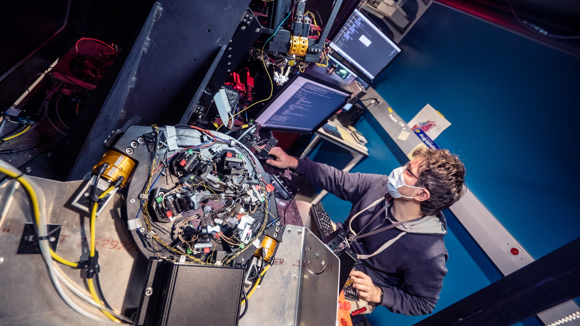Technician working on complex electronic equipment with exposed circuitry and wiring overhead view