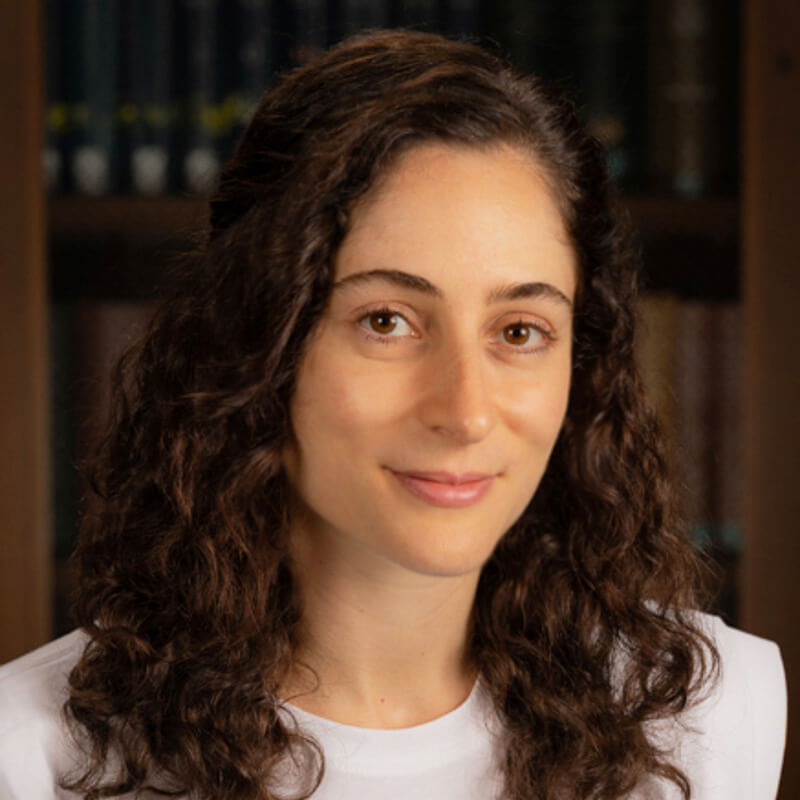 Portrait of a woman with long curly brown hair wearing a white shirt.