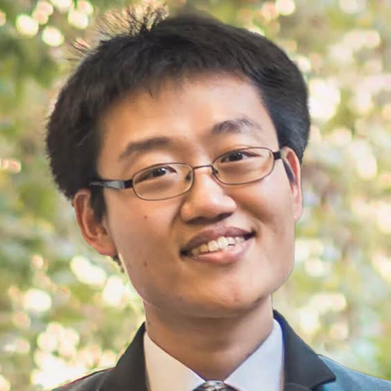 Smiling Asian man wearing glasses and business suit with blurred floral background