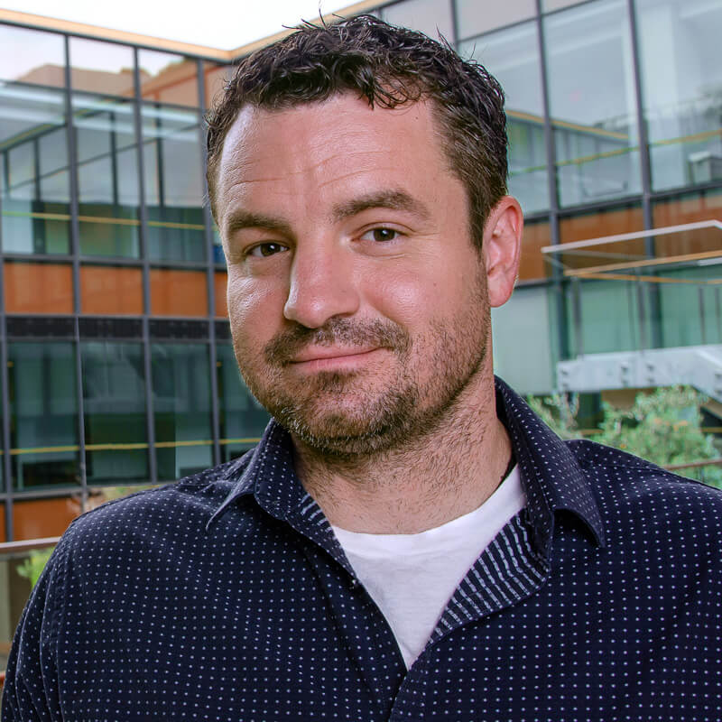Man with beard wearing dark polka dot shirt in front of modern building