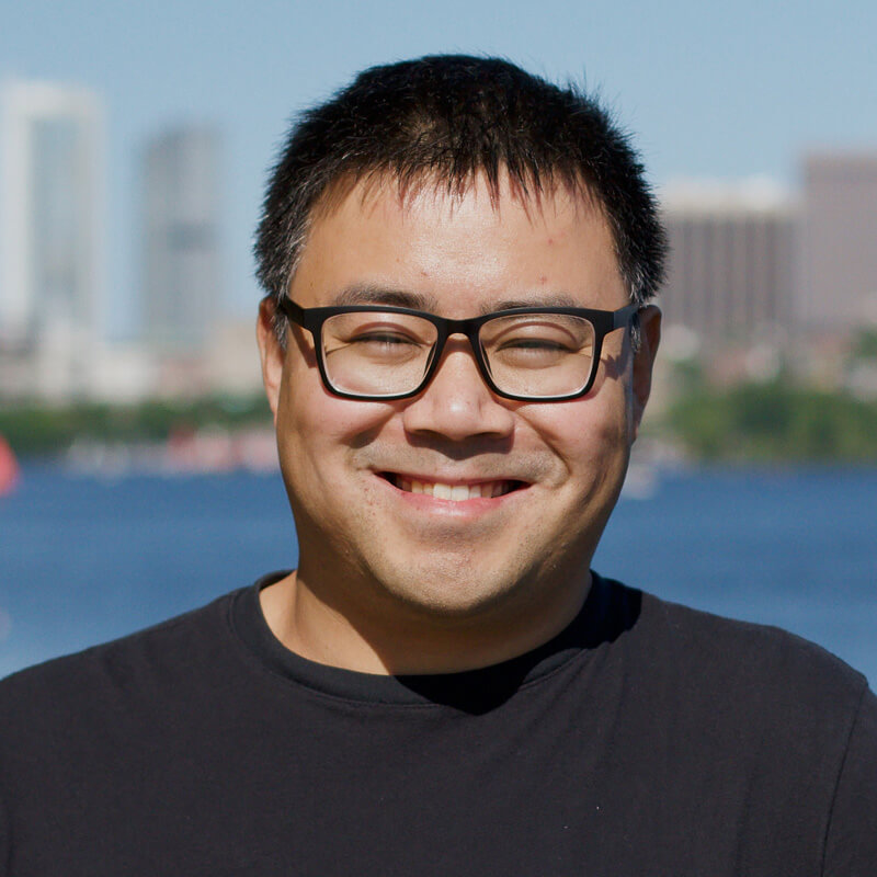 Man with glasses smiling outdoors with city skyline and water background