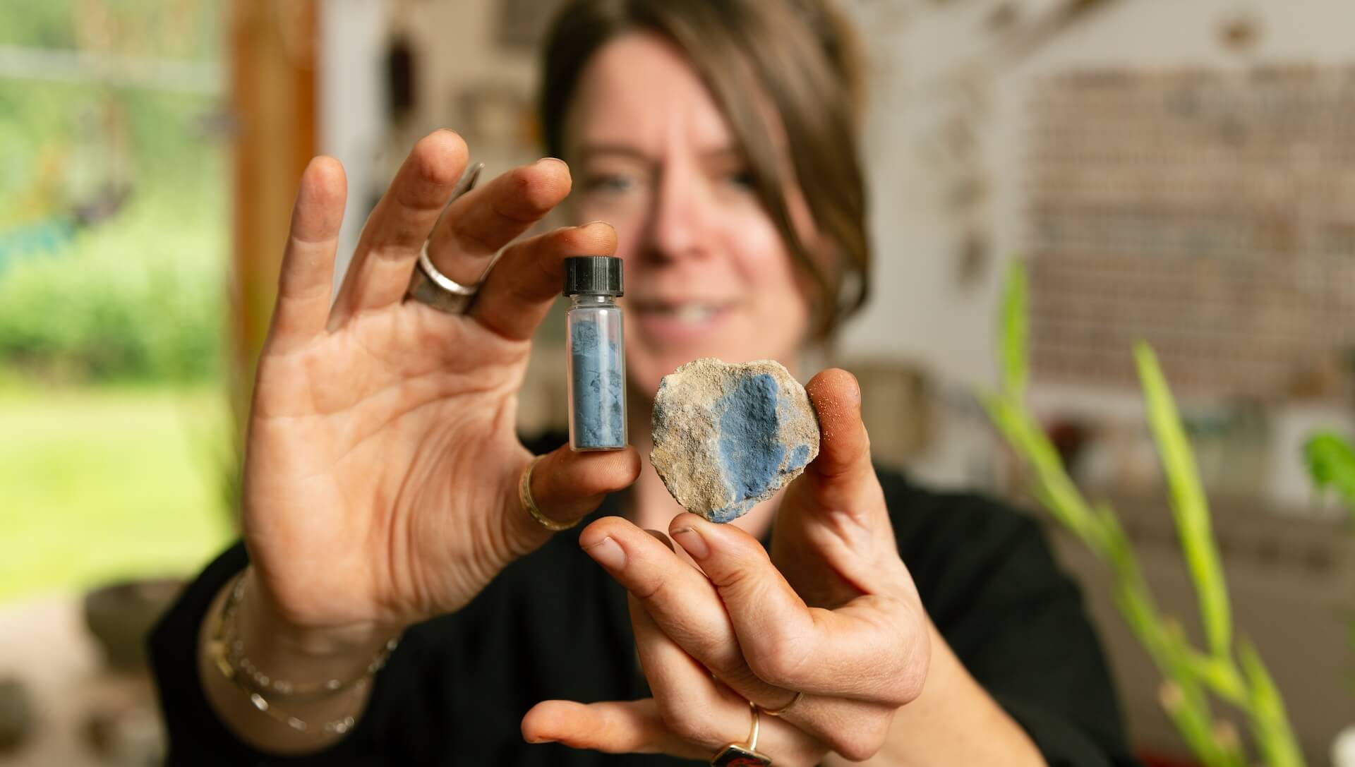 Woman holding rock sample and vial of mineral or sediment outdoors