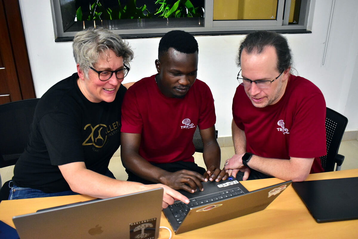 Three people collaborating at a table with laptops and a keyboard during a team training session.